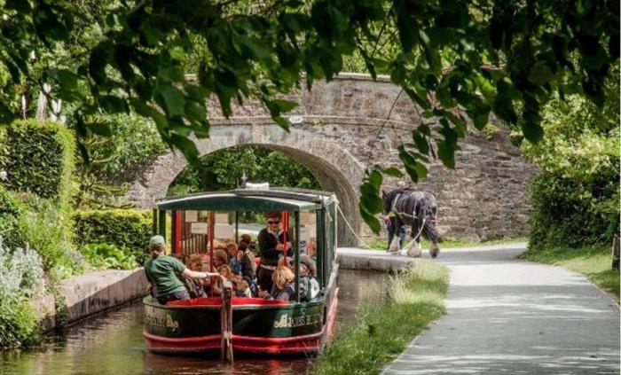 Scene of one of Llangollen Wharf's horse drawn boats travelling a long the Llangollen Canal heading to one of the historic stone bridges.